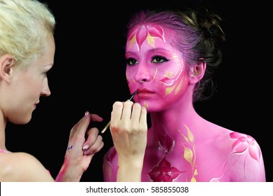Bodypaint master in work, paints a model for a photo shoot on black background