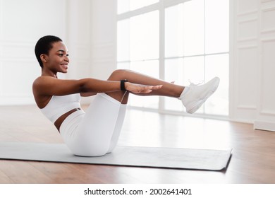 Bodyweight Workout Routine. Smiling young African American sportswoman doing v-ups abs exercises on floor yoga mat, doing crunches or sit-ups with raised legs and outstreched arms, working on six-pack