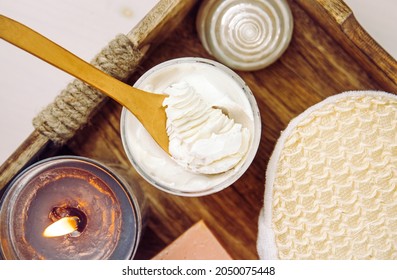 Bodywhip also known as body butter, skin care moisturizer cream on wood spoon and jar on natural wooden tray with bath sponge and candle.
