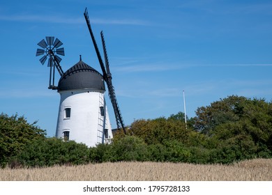 Bogense, Denmark-August 2020; Typical White Windmill For The Funen Area Close To Bogense With In The Foreground Growing Barley Against A Blue Sky