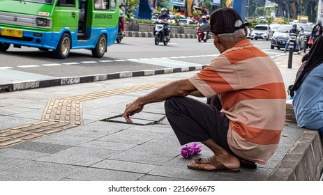 Bogor, Indonesia, 20 October 2022 : Old Man Resting While Squatting On The Sidewalk