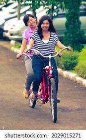 Bogor, Indonesia - May 2013: Portrait Of Young And Beautiful Asian Girls On Tandem Bicycle Ride In Street. Smiling Happy And Fun Expression. For Friendship And Together Concept.