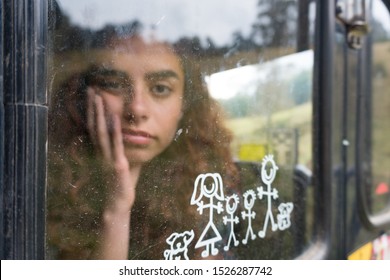 Bogota / Colombia - February 17 2019: Bored young girl inside a car. Picture of a happy family on the window. The redheaded might feel alone, sad and trapped. Holding head with hand. On the road.