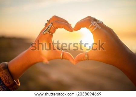 Bohemian chic gypsy woman wearing hands jewelry accessories and dress showing love sign. Boho detail close up at sunset.