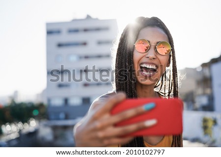 Bohemian girl doing selfie with mobile phone outdoor with city in background - Focus on face