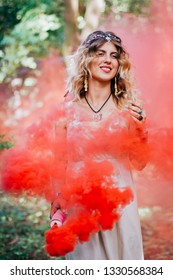 Bohemian Hippie Girl In The Forest.
Woman With Boho Style Jewelry.Colored Red Smoke On Background.Coachella Fashion Style Idea, Outfit .