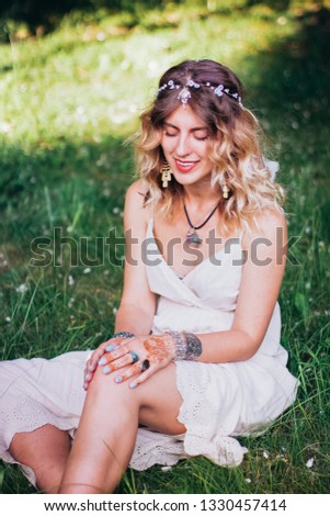 Bohemian hippie girl in white dress.
Woman hands with lot of boho style jewelry, blue rings,silver bracelets and henna tattoo. Summer day in forest.Outfit ideas for Coachella