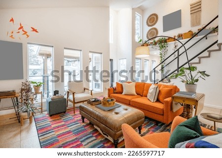 Bohemian style living room with orange sofa colored chairs books houseplants stair case and cluttered decor