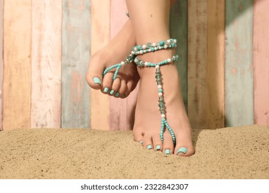 Boho barefoot sandals and anklet beaded jewelry. Close-up on the feet of a girl sitting on the beach, wearing decorative summer jewelry. Summer beach fashion trends.