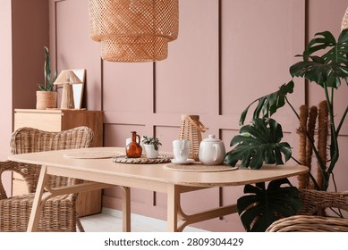 Boho chic dining room interior with wooden table, wicker chairs, and monstera plant against a pink wall