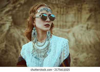 Boho Chic Fashion, Summer Style. A Beautiful Woman In Elegant Boho Style Jewelry And Trendy Sunglasses Stands Against The Backdrop Of Sand Dunes In A Desert.