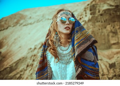 Boho Chic Fashion, Summer Style. A Beautiful Woman In Elegant Boho Style Jewelry With An Ethnic Headscarf On Her Head Stands Against The Backdrop Of Sand Dunes. 