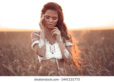 Boho chic style. Portrait of bohemian girl with white art posing over wheat field enjoying at sunset. Outdoors photo. Tranquility concept. Lifestyle. 