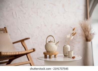 Boho and cozy interior of living room with rattan armchair, stylish coffee table, tea pot, vase with dried flowers, decoration and elegant accessories. Minimalist home decor. Template. 