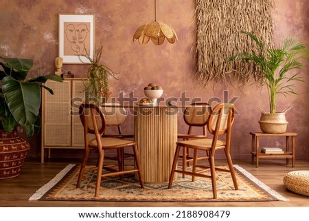 Boho and cozy interior of living room with poster mock up frame, round table, rattan chairs, commode, plants, decoration and accessories. Brown grunge wall. Template. Warm and oriental home decor.