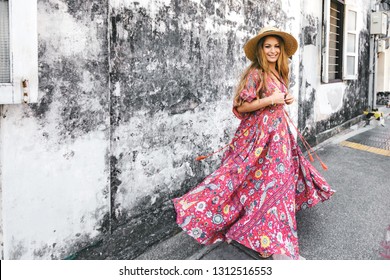 Boho girl in maxi dress and straw hat walking on the Asia city street. Travelling in Phuket Old Town in Thailand.