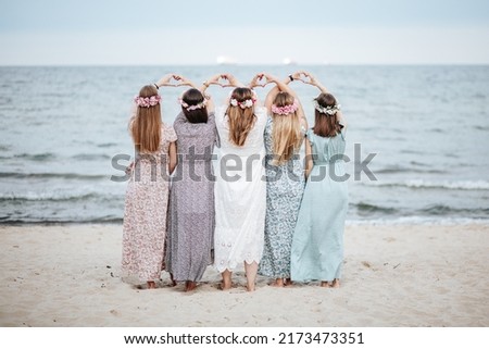 Boho hens party girls in long dresses  on the beach showing hearts shapes by hands.