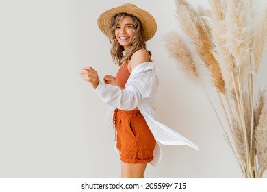 Boho mood. Stylish woman in summer outfit , straw hat  and orange clothes posing over white background in studio with pampas grass decor.