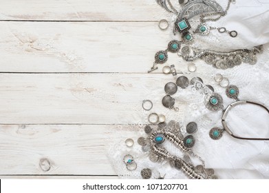 Boho style silver and turquoise jewelry set and white skirt with lace on vintage wooden background. Top view point.