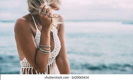 Boho styled model wearing white crochet crop top with tassels and silver jewelry on the beach