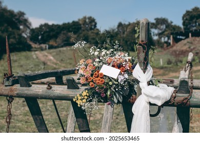 Boho summer wedding still life composition. Colorful floral bouquet with chrysathemum and eucalyptus flowers.Gift tag label mockup. Decorative rustic old wooden carriage. Blurred rural farm landscape.