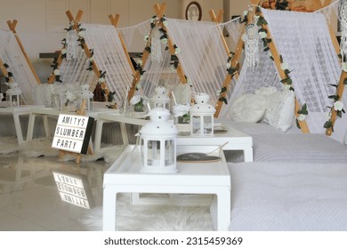 A boho themed girl's slumber party with white teepees, white lanterns, floral arrangement and white bedding.  - Powered by Shutterstock