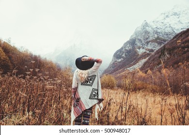 Boho Woman Wearing Hat And Poncho Standing By The Mountain. Cold Weather, Snow On Hills. Winter Hiking. Wanderlust.