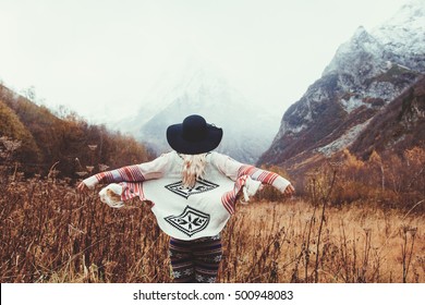 Boho Woman Wearing Hat And Poncho Standing By The Mountain. Cold Weather, Snow On Hills. Winter Hiking. Wanderlust.