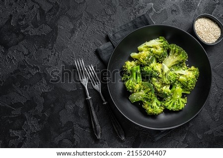 Boiled broccoli with spices in a plate. Black background. Top view. Copy space.