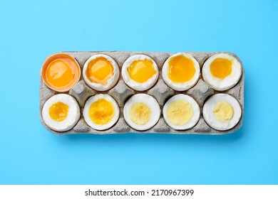 Boiled chicken eggs of different readiness stages in carton on light blue background, top view