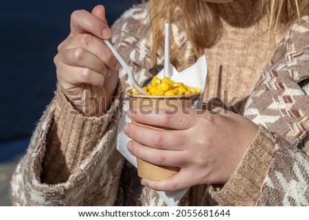 Boiled corn in a glass. Corn in the park. A woman is eating corn on a walk in the park. Snack on a walk.