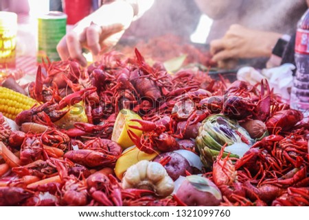 Boiled crawfish and vegetables piled on red checked tablecloth with eating tray and arm of person eating bokeh behind - shallow focus