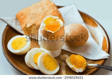 Boiled egg in egg cup, in shell and sliced on plate, spoon and bread (bun), towel., closeup. Healthy breakfast.