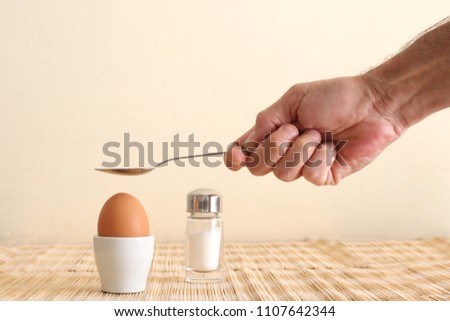 boiled egg in an eggcup and a man's hand holding a spoon