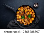 Boiled and fried potatoes in peels with champignon mushrooms and spices in frying pan. Black background, top view