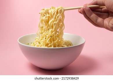 Boiled instant noodles on a pink background. Hand takes noodles with chopsticks for food. Fast food. Modern food. - Shutterstock ID 2172938429