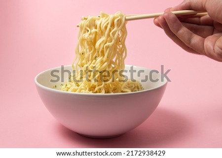 Boiled instant noodles on a pink background. Hand takes noodles with chopsticks for food. Fast food. Modern food.