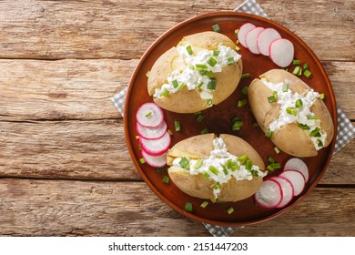 Boiled jacket potatoes stuffed with cottage cheese, sour cream and green onions close-up in a plate on a wooden table. Horizontal top view from above