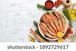 Boiled langoustines with parsley and spices on a plate. Norway lobster on a white wooden background. Top view. Free copy space.