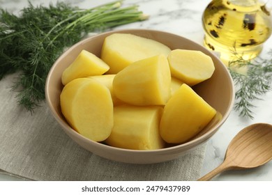 Boiled potatoes in bowl, dill, oil and spoon on white marble table