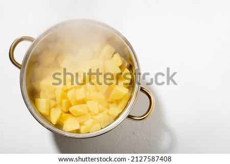 Boiled potatoes in a pot. Hot potato cubes with a piece of butter. Cooking boiled potatoes, mashed potatoes. Steam is coming. White background.