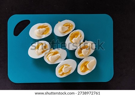 Boiled and raw eggs on a green cutting board, some sliced with mayonnaise. Food preparation concept in natural light.