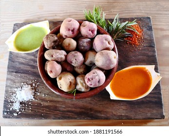 Boiled "wrinkled" potatoes prepared following canarian recipe on wooden plate and two red and green local dressings "mojo" in a restaurant in Teguise city in Lanzarote, Canary islands. Selective focus - Shutterstock ID 1881191566