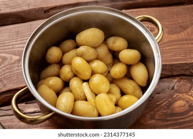 Boiled young small potatoes in a saucepan on a wooden background. - Powered by Shutterstock