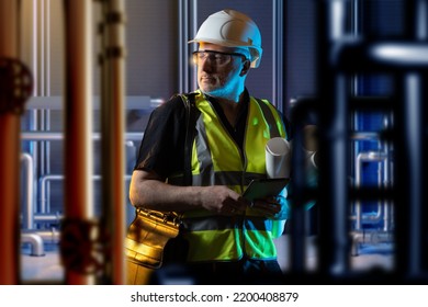 Boiler Room Engineer. Man Among Pipes. Human In Engineers Clothes Is Standing Indoor. Guy In Room With Utilities. Boiler Room Design Concept. Worker With Tablet Among Boiler Equipment. Art Focus.