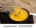 Boiling corn flour in a cast iron pot, making mamaliga, traditional romanian food, and mixing with a stainless steel whisk, soft focus close up