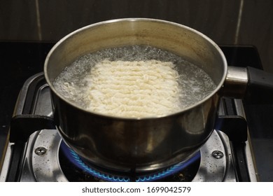 Boiling Instant Noodle In Plain Water Inside Hot Metal Pot On Burning Blue Flame From Gas Stove