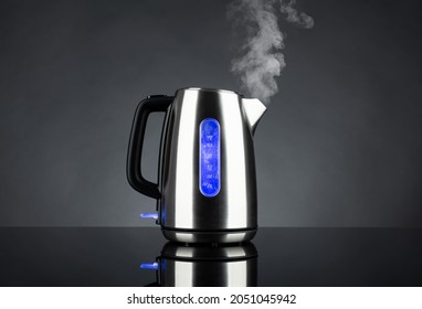 Boiling steel electric kettle with light and steam with reflection, on black background 