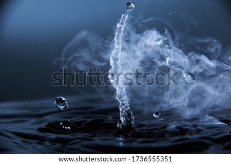Boiling water splash with steam on dark blue background closeup.