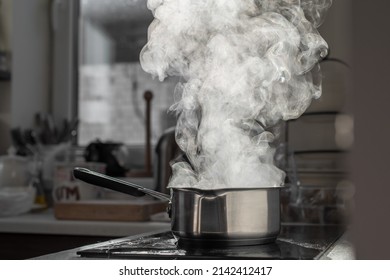 Boiling water with steam in a pot on an electric stove in the kitchen. Blurred background, selective focus.